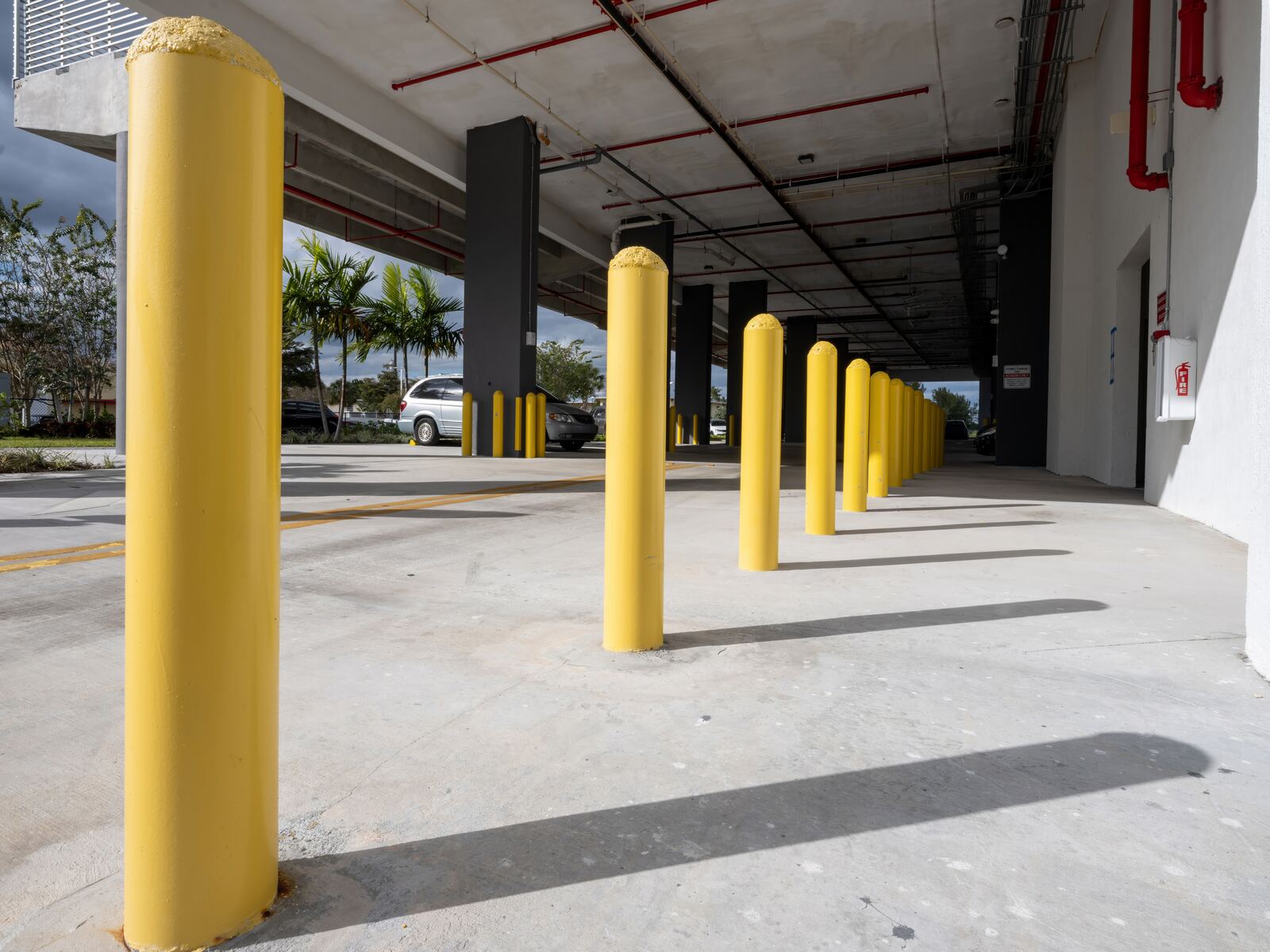 Row of yellow steel safety bollards set in concrete at a commercial parking structure