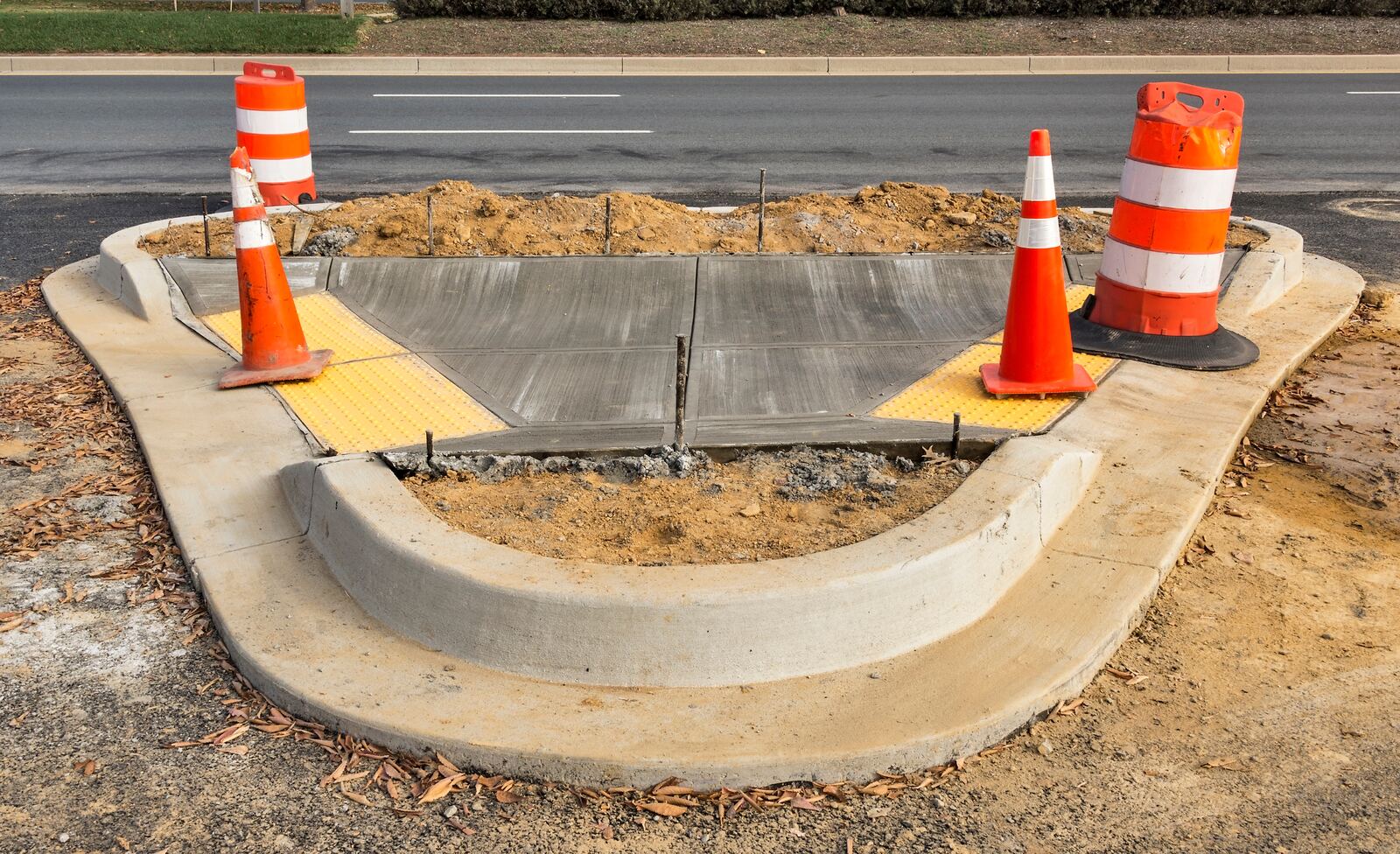 New ADA concrete curb ramp with yellow detectable warning pads at a street corner