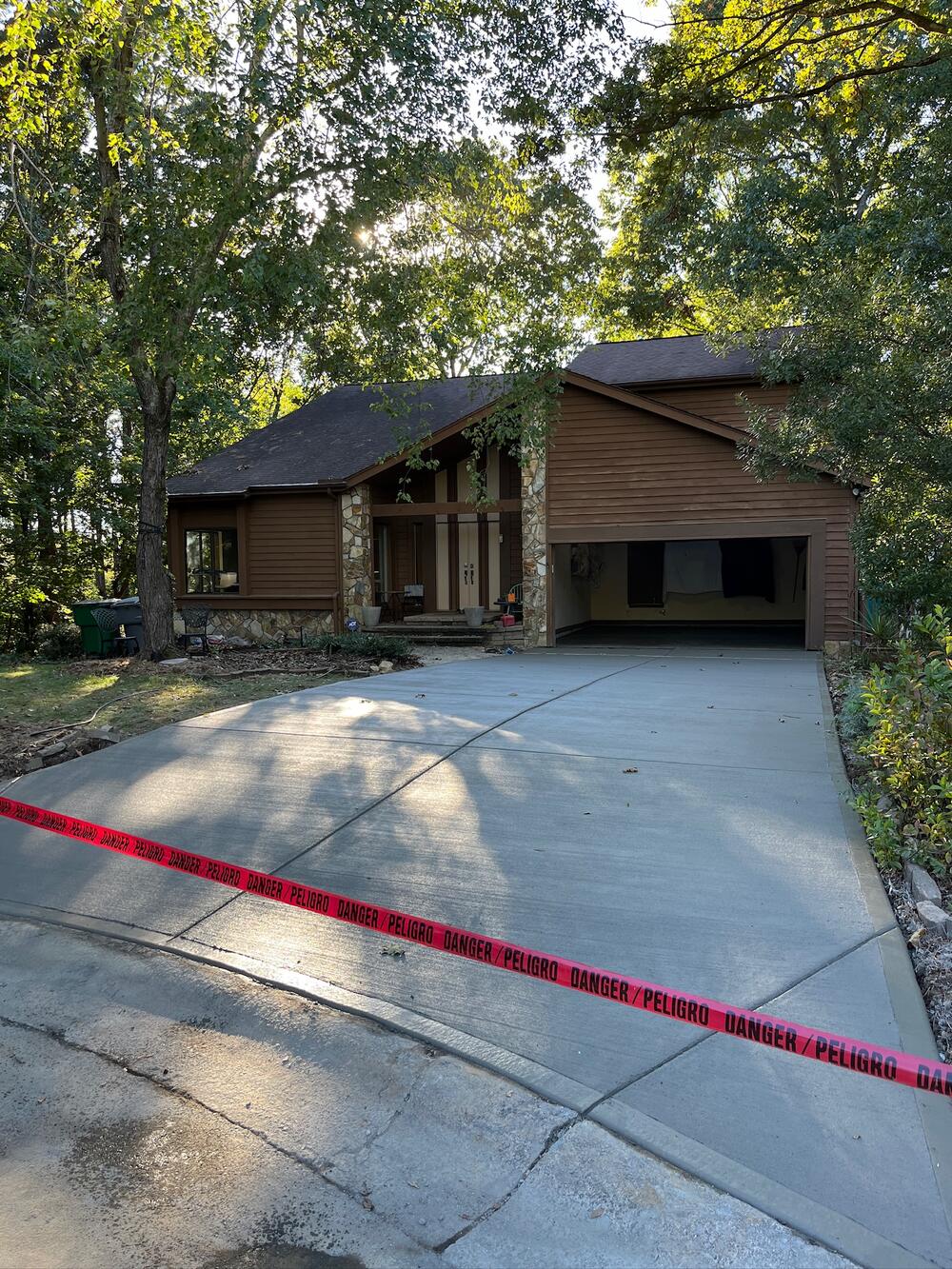 New concrete driveway with caution tape in front of a wood and stone house
