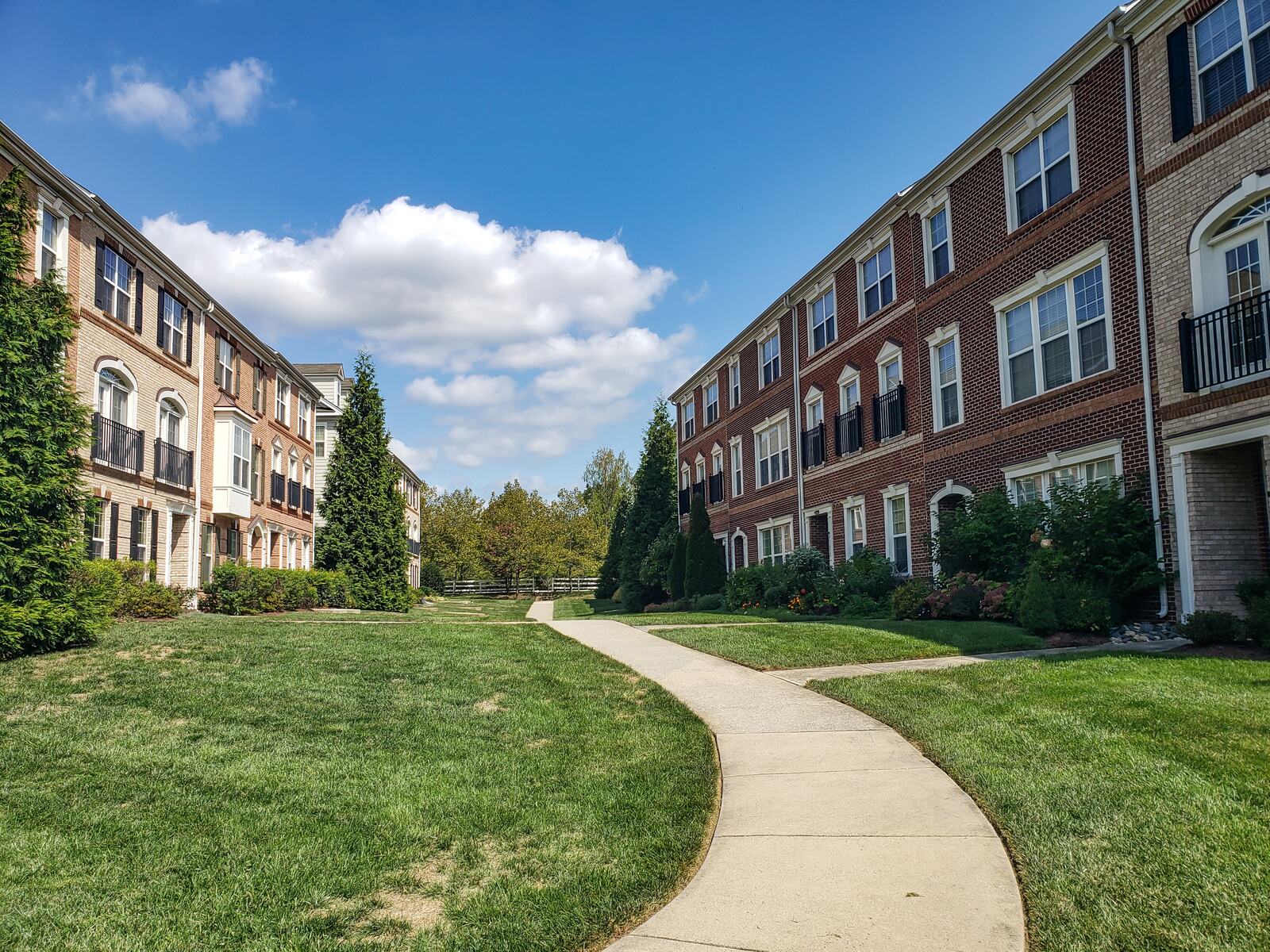 Wide concrete community path curving past an apartment building